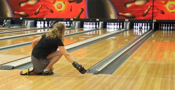 A woman throws a bowling ball on the track in order to knock down the pins.