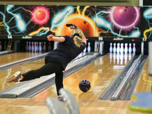 A woman throws a bowling ball on the track in order to knock down the pins.