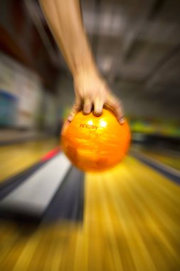 Bir adamın eli turuncu bir bowling topunu tutuyor ve bowling salonuna atıyor. Bulanık hareket.
