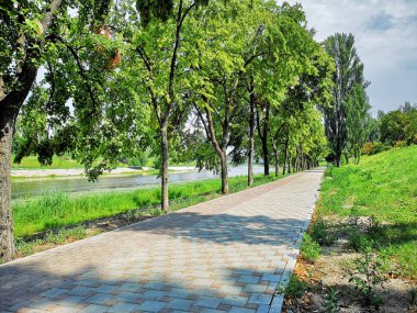 Nehir boyunca fayans yolu. Ağaçlar ve otlar büyür.