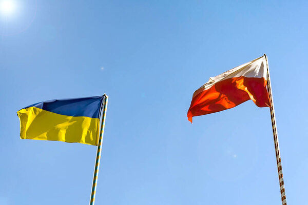 Flags of Ukraine and Poland. Two flags on the background of a beautiful blue sky and green trees.