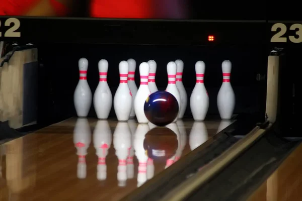 Bowling ball rolls down the track and is next to the skittles in white.