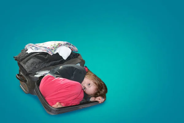 子供は物事が折り畳まれているスーツケースに横たわっています 物事や服の旅行やスタイリングの概念 青い背景で — ストック写真