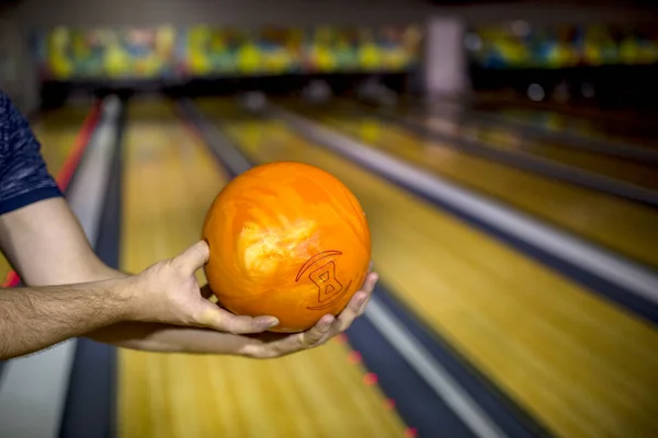 男の手には ボウリング場にそれを投げる準備ができて オレンジ色のボウリングボールを保持しています — ストック写真