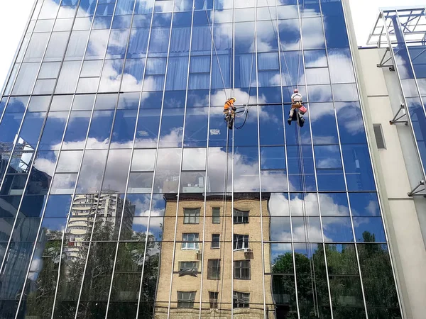 İki çalışan dağcı yüksek katlı bir binanın cam duvarında, alt manzaralı.
