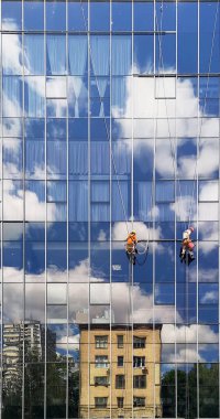 Çalışan iki dağcı yüksek katlı bir binanın cam duvarı üzerinde çalışıyorlar.