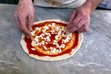 Pizza pişiriyorum. Ketçap soslu pizza için gözleme masada duruyor. Aşçının elleri pizza malzemelerini istifliyor..