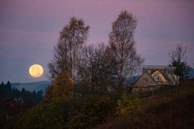 Tepelerde kocaman bir ay. Köyün ve çiftlik evinin üzerinde ay doğuyor. Süper Ay.
