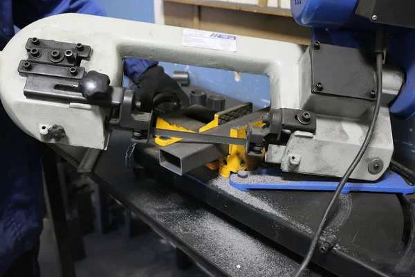 band saw cutting tool steel bar by automatic feed. Iron disc. Worker cuts off a piece of iron profile