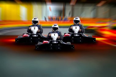 Three riders Go kart speed rive indoor race on the background of the track. Go kart indoor, cart racing fast, car where gokarting, we speed racing, racers banner Copy space. clipart