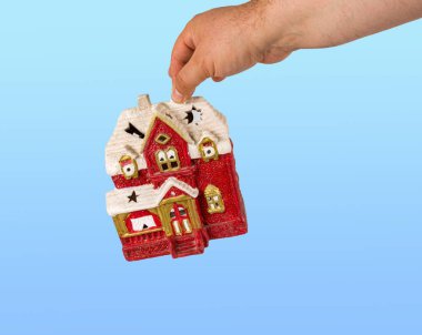 Elleri kırmızı renkli oyuncak evi tutuyor. Ev ulaşımı konsepti. Hareketli binalar. Mavi bir arkaplanda.