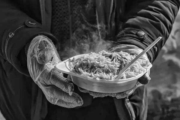 Food for the homeless. Street food. Plate with pilaf in hands in disposable gloves. Black and white image.