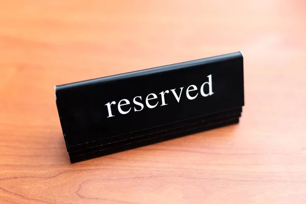 Reserved table. The black white tag is placed on a wooden table. Reserved logo. Booking sign. Plastic tag with booking logo. Restaurant Reserved Table