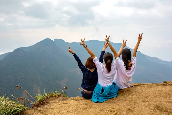 Dağlarda gezici turizm. Üç kız elleri yukarıda, uçurumun kenarında oturuyorlardı. Manzaranın tadını çıkarın. Dünyanın sonu Sri Lanka.
