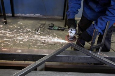 Öğütücü metal. Öğütücü tekerlek. Çilingir, atölyede kaynak yaptıktan sonra demir köşeyi temizler. Kıvılcımlar uçuşuyor.