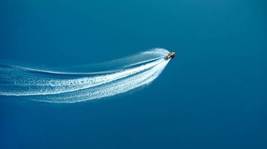 Jet ski mavi suda büyük bir hızla ilerliyor, köpüklü bir iz bırakıyor. Yukarıdan görüntüle