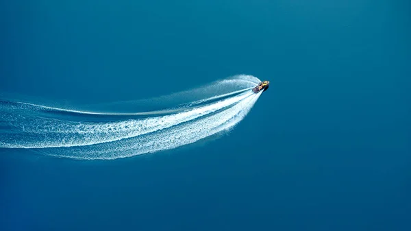 The jet ski travels at great speed through blue water, leaving a foamy trail. View from above