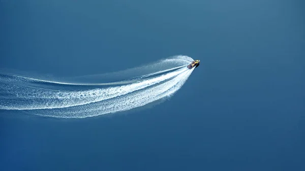 The jet ski travels at great speed through blue water, leaving a foamy trail. View from above