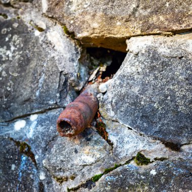 An old rusty pipe sticks out of a stone wall. Impotence, genital diseases in men concept. The tube looks like an old sore penis.