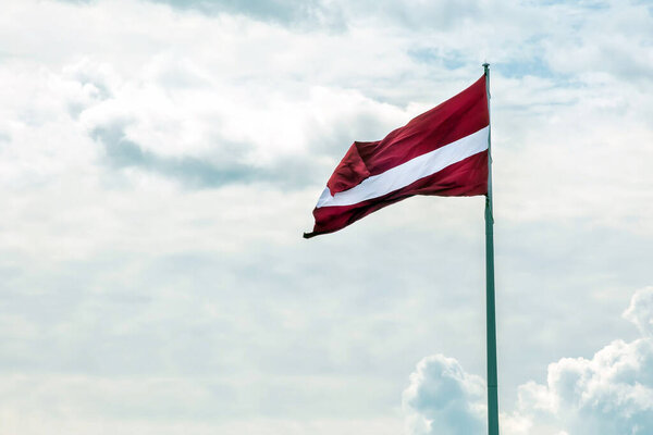Flag of Latvia on a long flagpole against the sky. Red-white flag.