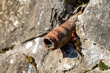 An old rusty pipe sticks out of a stone wall. The tube looks like an old sore penis. Impotence, genital diseases in men concept.