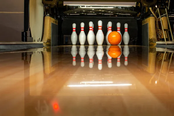 White bowling pins and an orange ball on a bowling alley. Beautiful reflection. Close-up. Front view.