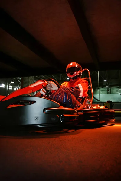 The racer is sitting on a go-kart, lights are burning above him. Place for an inscription. Photo in the dark