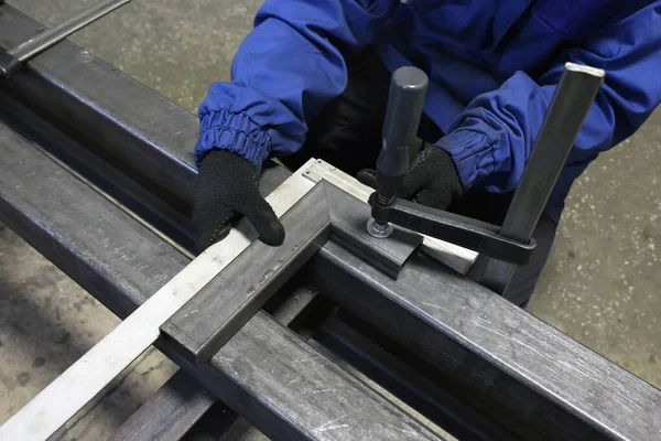 The worker measures the right angle for the iron billet clamped in a vice. Preparation with welding.