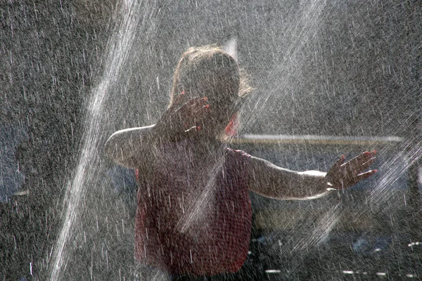 晴れた日に噴水で女の子が入浴します 噴水からのスプレー滴は若い女の子をリフレッシュします 暑い夏の日の女の子と噴水 — ストック写真