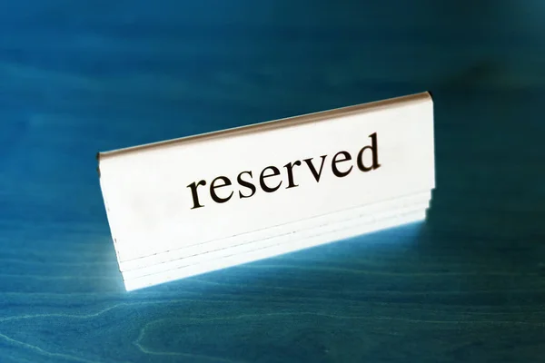 Reserved table. The black white tag is placed on a wooden blue table. Reserved logo. Booking sign. Plastic tag with booking logo. Restaurant Reserved Table