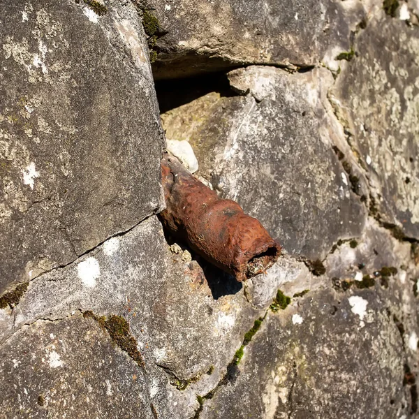 An old rusty pipe sticks out of a stone wall. Impotence, genital diseases in men concept. The tube looks like an old sore penis. — Stock Image Old Rusty Pipe Sticks Out Stone Wall Impotence Genital Diseases Royalty Free Stock Photos