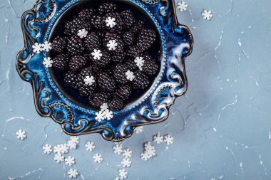 Mavi bir arka plan üzerinde olgun böğürtlen ile Kase, şeker kar taneleri ile