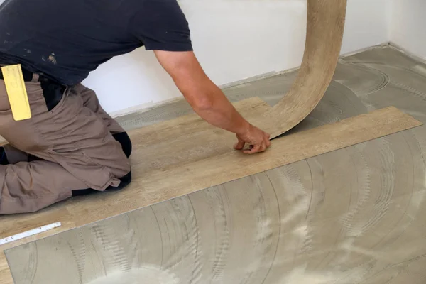 Trabajar en la colocación de suelos. Trabajador instalación de piso de baldosas de vinilo nuevo . — Foto de Stock