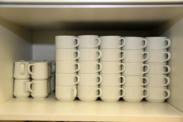 В шкафу стоят стопки белых кофейных кружек — стоковое фото