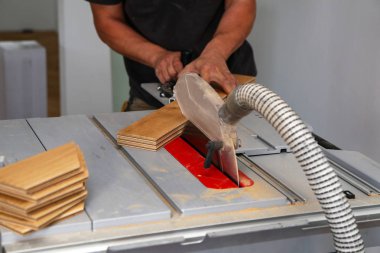 İşçi, parkeyi dairesel testere ile elle kesiyor.