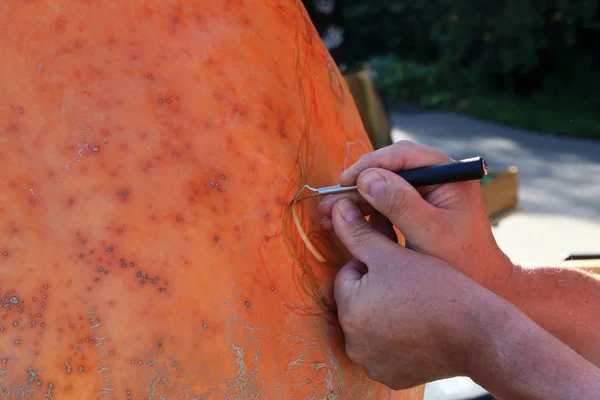 Mans hands close-up carve pumpkinat the autumn holiday