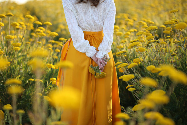 A girl in a yellow skirt and white blouse stands in a field of yellow flowers
