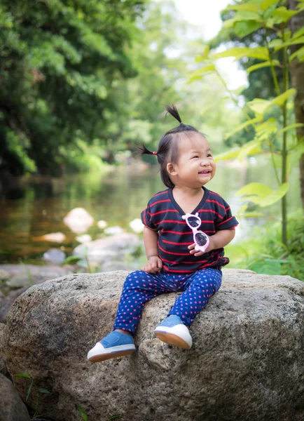 背景の川の岩の上に座って微笑んでいる子女の子 — ストック写真