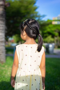 Parkta yürüyen güzel saçlı sevimli küçük bir kızın arka manzarası.