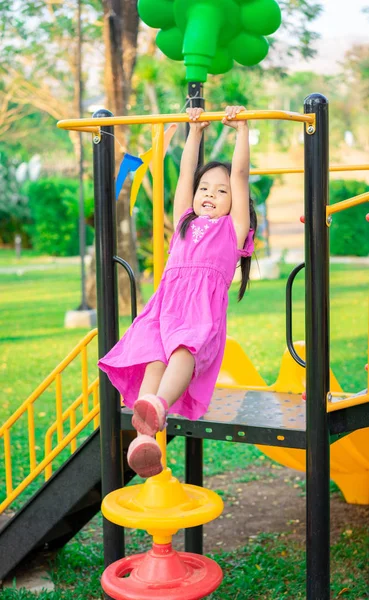 Милая азиатская маленькая девочка висит на горизонтальной панели во время игры Лицензионные Стоковые Фото