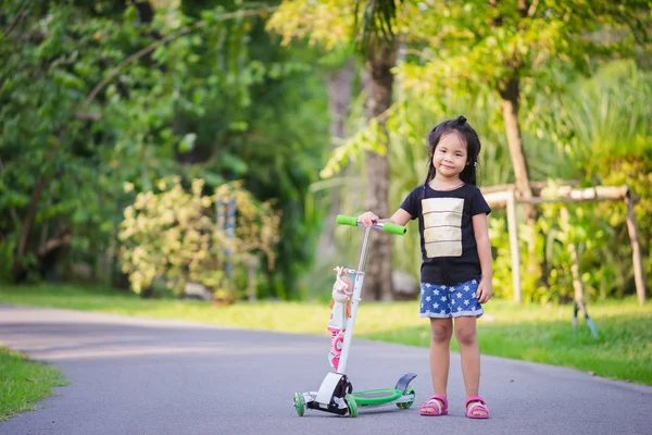 Portrait of cute little asian girl and scooter in a park — Stock Photo, Image