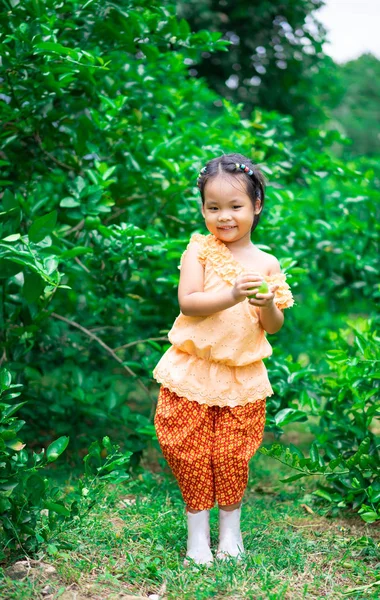 Happy little girl in Thai period dress holding lime fruit in her — Stock Photo, Image