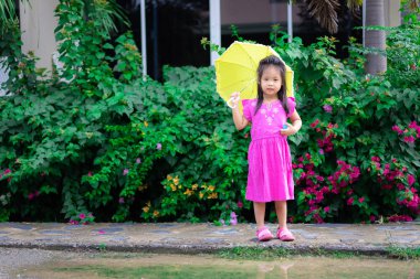 yağmur gününde sarı şemsiyeile pembe elbiseli küçük kız