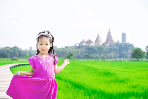 Petite fille sur le pont dans le champ vert avec fond de temple — Photo