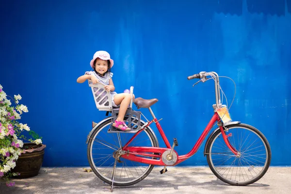 Felice bambina cavalcare una bicicletta nel parco con backgroun blu — Foto Stock