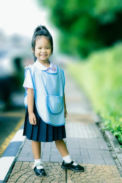 Porträtt av lycklig liten flicka i thailändsk skoluniform stående på — Stockfoto