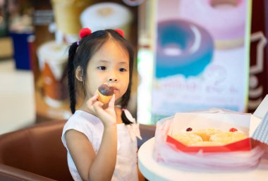 Küçük asyalı kız tutarak ve d yeme ile sandalyede oturan