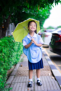 Tayland okul üniformalı küçük bir kız. Yağmurlu bir günde sarı şemsiyeli.