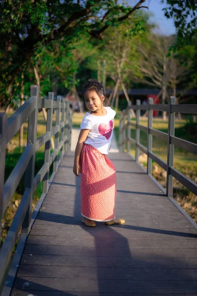 Mutlu Asyalı küçük kızın portresi Tahta köprüde güneş ışığıyla duruyor