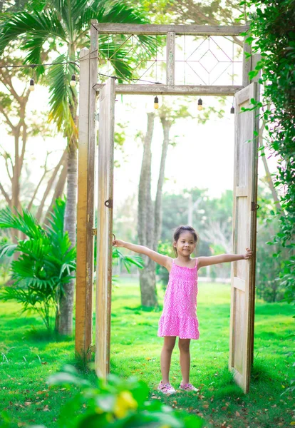 Kleines Asiatisches Mädchen Steht Einer Großen Holztür Zum Garten lizenzfreie Stockbilder